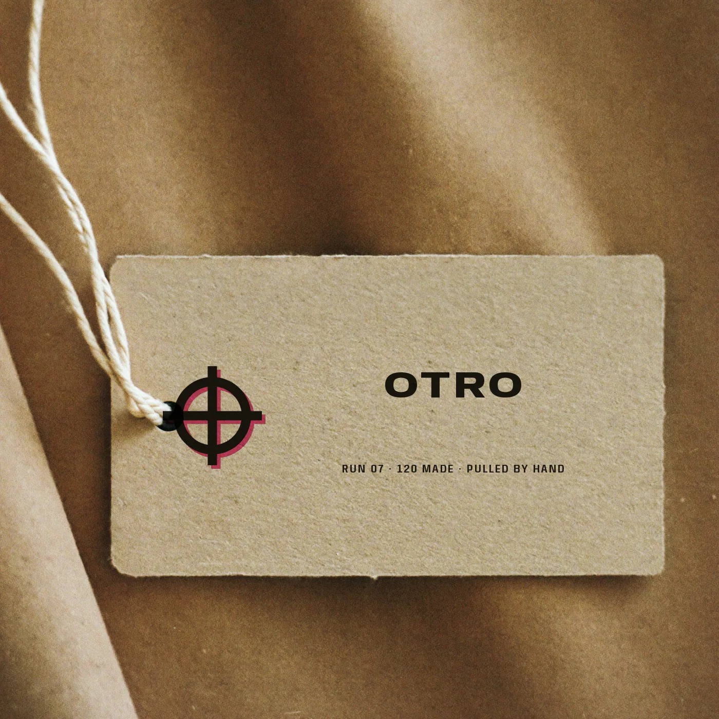 A sand cardboard swing tag printed with the OTRO target, the wordmark and the run number
